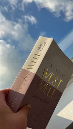 a person holding up a book in front of a blue sky with some clouds behind it