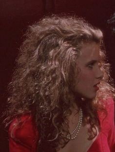 a woman with long curly hair standing next to a man in a red shirt and tie