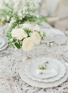 the table is set with white plates and flowers