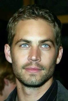 a close up of a person wearing a suit and tie with blue eyes looking at the camera