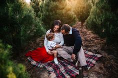 a man and woman sit on a blanket in the middle of an orchard with their child