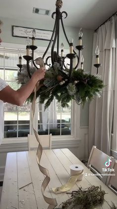 a man is decorating a chandelier with greenery and candles on the table