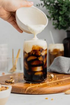 a person pours milk into a glass filled with ice and nuts on a cutting board