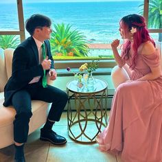 a man and woman sitting on couches in front of a window with ocean view