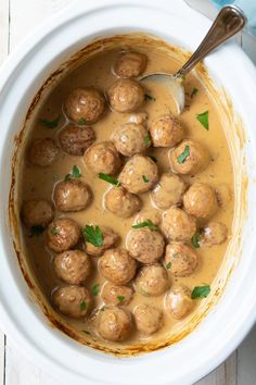 a white bowl filled with meatballs covered in gravy and garnished with parsley