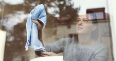 a woman wiping her hands with a blue towel in front of a window, looking out the window