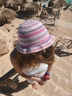 a woman wearing a pink and white crocheted hat looking down at the beach