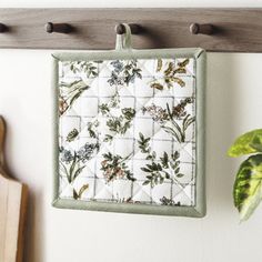 a pot holder hanging on the wall next to a cutting board with a plant in it