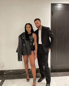 a man and woman standing next to each other in front of a door wearing black outfits