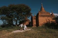 two people walking down a path in front of an old brick building with spires