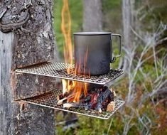 a cup is sitting on top of a metal shelf next to a fire in the woods