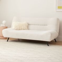 a white couch sitting on top of a wooden floor next to a lamp and rug