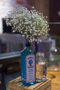 a blue bottle with baby's breath in it sitting on a wooden box next to a glass vase