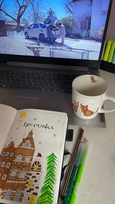 a laptop computer sitting on top of a desk next to a cup and pencils