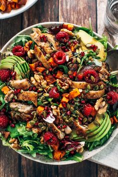 a salad with chicken, raspberries, avocado and nuts on top