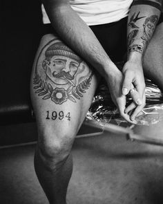 black and white photograph of a man with tattoos on his legs holding the leg of another person