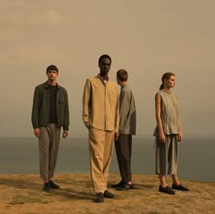 three men and two women standing on top of a hill next to the ocean with an airplane in the sky