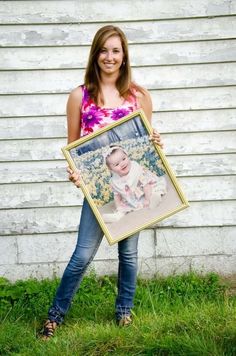 a woman holding up a framed photo in front of a white house with the caption,