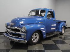 an old blue truck is parked on a checkered floor