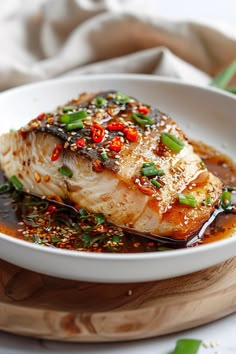 a white plate topped with fish covered in sauce and garnished with green onions