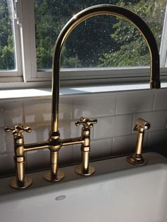 a kitchen sink with two brass faucets in front of a window