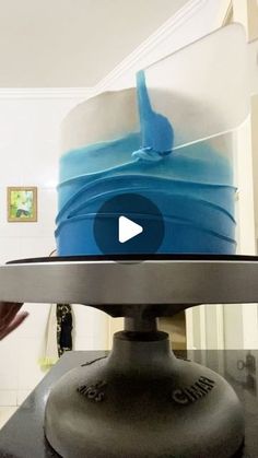 a blue and white cake sitting on top of a metal stand in front of a mirror