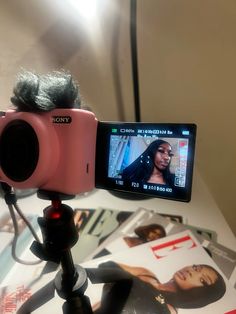 a pink camera sitting on top of a tripod next to a pile of magazines