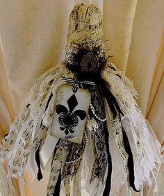 an old fashion doll is hanging on the curtain with black and white lace around it