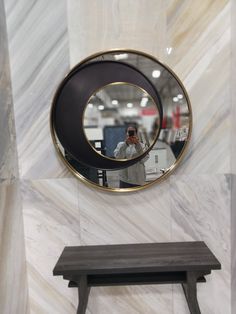 a person taking a selfie in front of a round mirror on a wall next to a bench