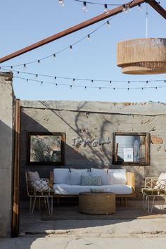 an outdoor living area with white furniture and string lights hanging from the ceiling over it