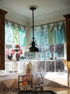 a kitchen sink sitting under a window covered in blue and green curtains