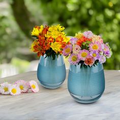 two blue vases filled with colorful flowers on top of a table