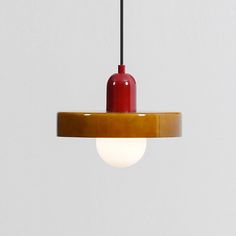 a red and yellow light hanging from a ceiling fixture with a white wall in the background