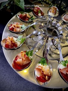 spoons filled with different types of food on top of a metal tray and surrounded by greenery