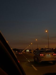 cars driving down the road at night with street lamps on either side and one car in the foreground