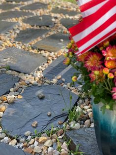 flowers and an american flag in a vase on a stone path with flags at the end