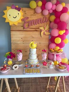 a table topped with a cake and lots of balloons next to a wooden sign that says smile