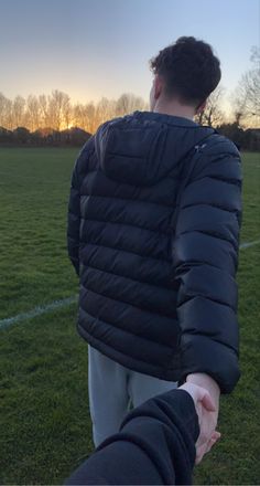 two people holding hands on a soccer field with the sun setting in the distance behind them