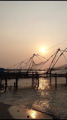 the sun is setting over some fishing nets in the water on the beach near an ocean pier