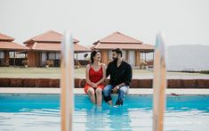 a man and woman sitting on the edge of a swimming pool