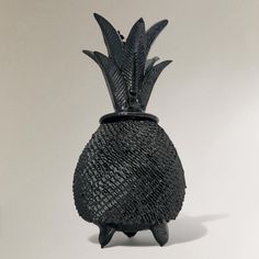 a black vase with a pineapple design on the top and bottom, sitting on a white surface