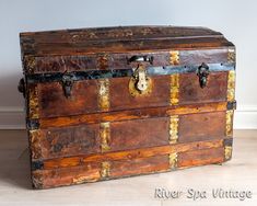 an old trunk is sitting on the floor in front of a white wall and wooden floors