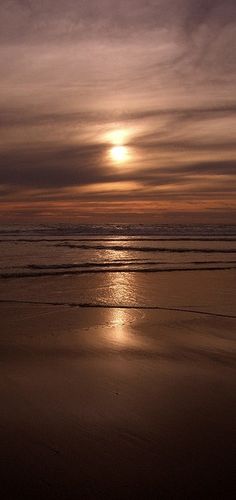 the sun is setting over the ocean with some clouds in the sky and one person walking on the beach