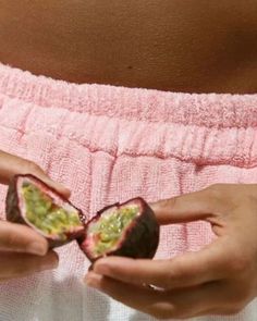 a pregnant woman holding two pieces of fruit in her hands while wearing a pink towel