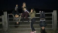 three young women hanging out in front of a fence