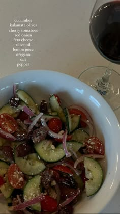 a white bowl filled with cucumbers and onions next to a glass of wine