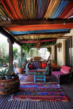 an outdoor covered porch with colorful rugs and pillows on the floor, potted plants