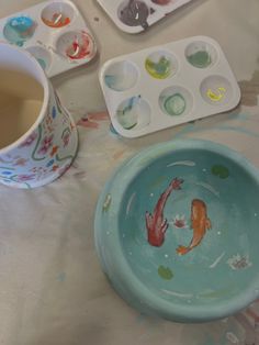 there is a blue bowl with two gold fish in it next to some paint trays