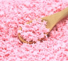 a wooden spoon filled with pink sprinkles on top of a bed of pink powder