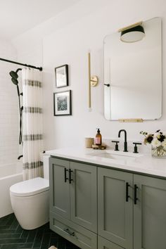 a white bathroom with gray cabinets and black tile flooring on the walls, along with a large mirror over the sink